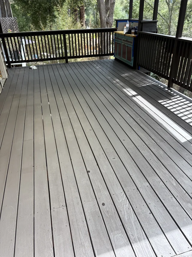 A finished grey wood deck bordered by timber railings and trees.